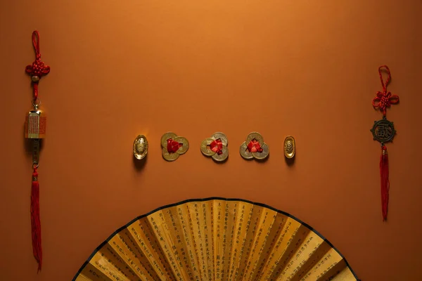 Decoraciones tradicionales chinas doradas y abanico con jeroglíficos sobre fondo marrón - foto de stock