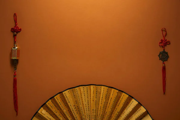 Vue de dessus du ventilateur doré avec hiéroglyphes et décorations chinoises traditionnelles sur fond brun — Photo de stock