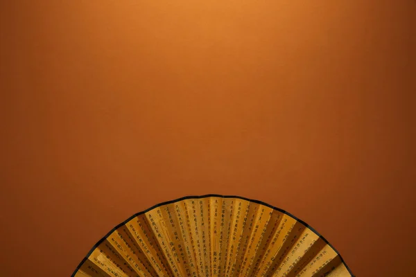 Top view of traditional golden chinese fan with hieroglyphs on brown background — Stock Photo