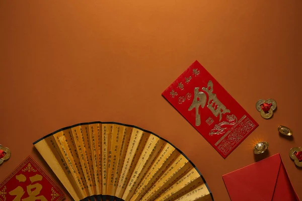 Top view of chinese new year composition with golden decorations and fan with hieroglyphs on brown background — Stock Photo