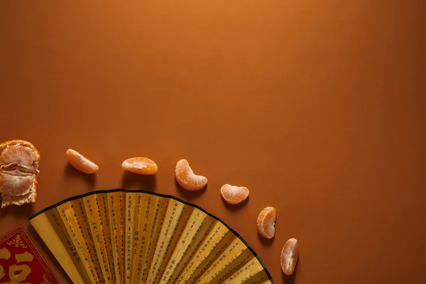 Вид зверху на золотий вентилятор з ієрогліфами і очищеним мандарином на коричневому фоні — стокове фото