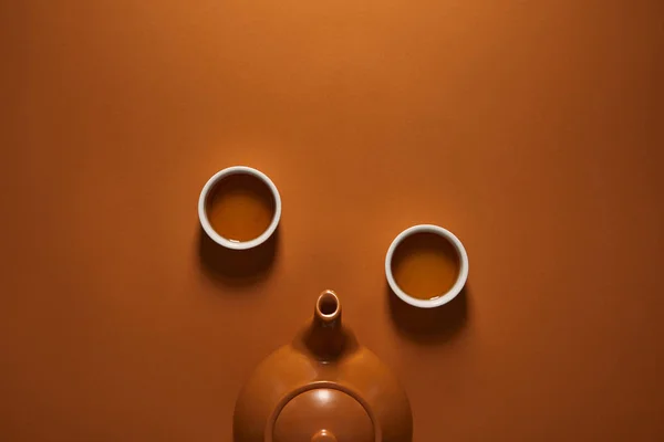 Vue de dessus de la théière chinoise en céramique brune et des tasses de thé sur fond brun — Photo de stock