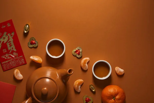 Vue de dessus de l'ensemble de thé, mandarines et décorations chinoises traditionnelles sur fond brun — Photo de stock