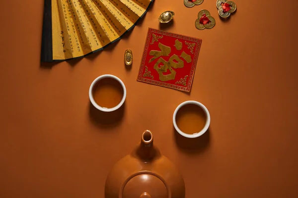 Top view of tea set, fan with hieroglyphs and traditional chinese decorations on brown — Stock Photo