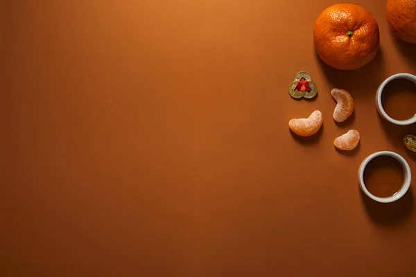 Top view of fresh ripe tangerines, cups of tea and golden coins on brown background, chinese new year composition — Stock Photo