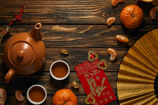 Vista superior do ventilador com hieróglifos, decorações chinesas douradas, conjunto de chá e tangerinas na mesa de madeira — Fotografia de Stock