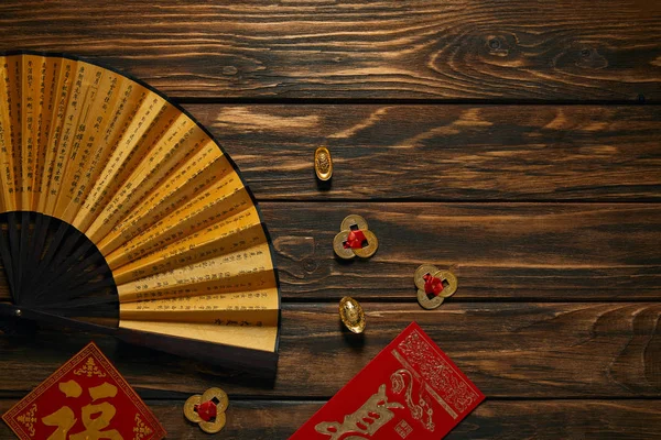 Top view of fan with hieroglyphs and golden chinese decorations on wooden table — Stock Photo