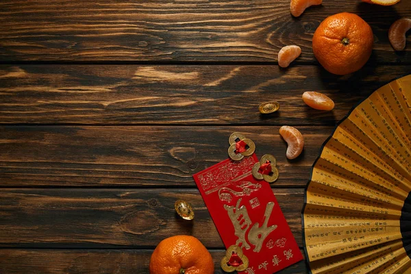 Vista dall'alto di mandarini freschi maturi, ventaglio con geroglifici e monete d'oro sul tavolo di legno — Foto stock