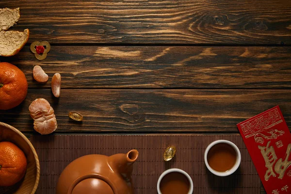 Top view of teapot, cups of tea, fresh ripe tangerines and traditional chinese decorations on wooden table — Stock Photo