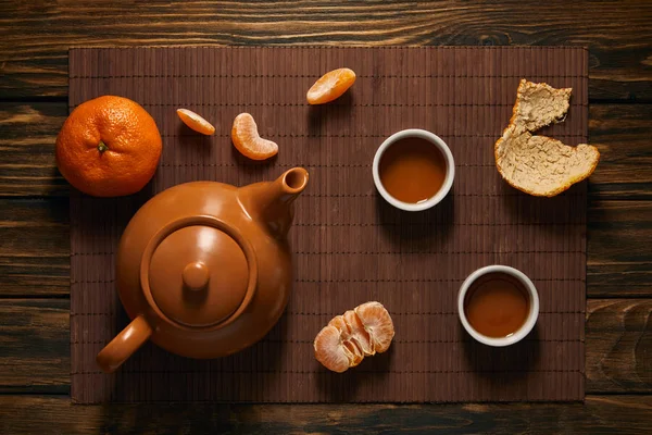 Draufsicht auf Teekanne, Tassen Tee und Mandarinen auf Bambusmatte — Stockfoto