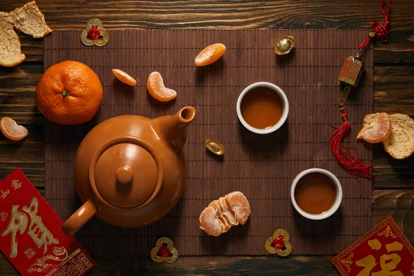 Top view of tea set, tangerines and traditional chinese decorations on bamboo mat — Stock Photo
