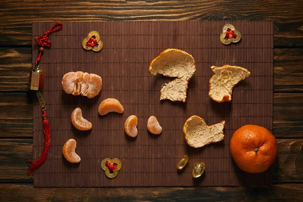 Vue de dessus de mandarines entières et pelées avec des décorations traditionnelles chinoises dorées sur tapis de bambou — Photo de stock