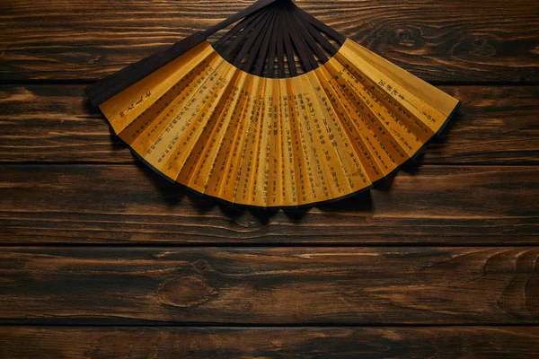 Top view of decorative black and golden fan with hieroglyphs on wooden surface — Stock Photo