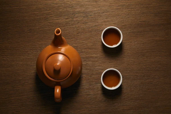 Vista superior de la tetera china de cerámica marrón y tazas de té en la mesa de madera - foto de stock