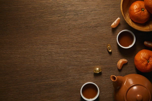 Верхний вид чайного сервиза, свежие спелые мандарины и традиционные золотые китайские украшения на деревянном столе — стоковое фото