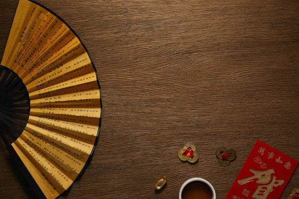 Top view of fan with hieroglyphs, golden coins and cup of tea on wooden table — Stock Photo