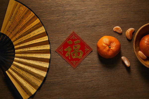 Vue de dessus du ventilateur, mandarines fraîches mûres et hiéroglyphe doré décoratif sur table en bois — Photo de stock