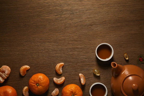 Верхний вид чайного сервиза, мандаринов и монет на деревянную поверхность — стоковое фото