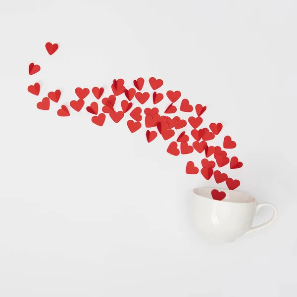 Vue du dessus de la tasse et tas de coeurs coupés en papier rouge sur fond blanc — Photo de stock