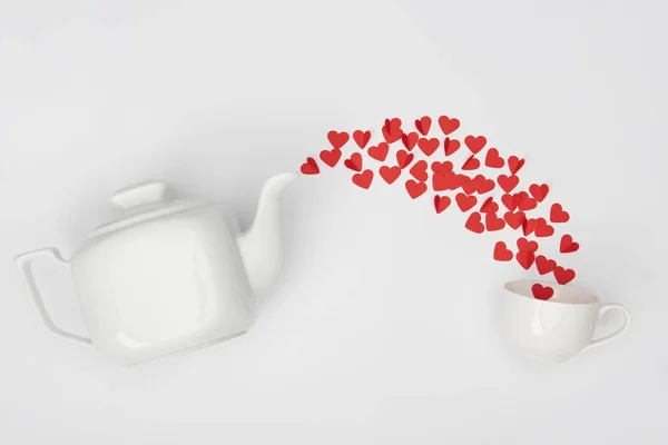 Top view of tea pot, cup and heap of red paper cut hearts on white background — Stock Photo