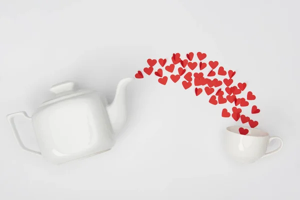 Vista superior de la tetera, taza y montón de corazones cortados de papel rojo sobre fondo blanco - foto de stock