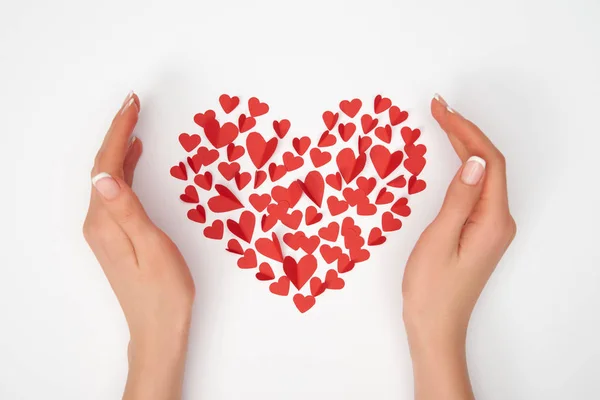 Vista recortada de las manos femeninas cerca de la disposición en forma de corazón de pequeños corazones cortados de papel rojo — Stock Photo