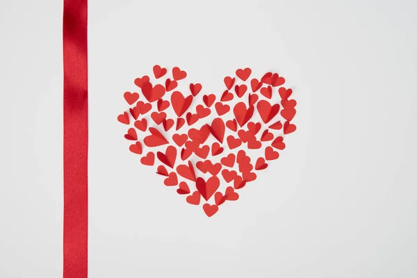 Herzförmige Anordnung kleiner roter papiergeschnittener Herzen mit Satinband auf weißem Hintergrund — Stockfoto