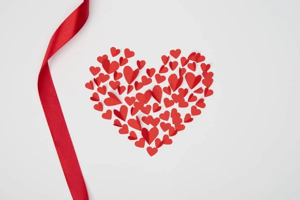 Arranjo em forma de coração de pequenos corações de papel cortado com fita vermelha ondulada no fundo branco — Fotografia de Stock