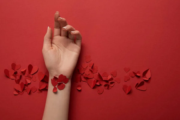 Vista cortada da mão feminina com papel cortar corações decorativos no fundo vermelho — Fotografia de Stock