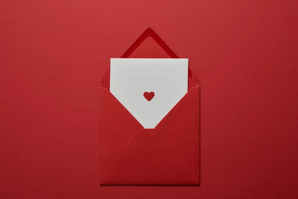 Vue du dessus de la lettre blanche avec coeur dans l'enveloppe sur fond rouge — Photo de stock