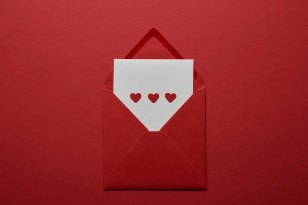 Top view of white letter with hearts in envelope on red background — Stock Photo