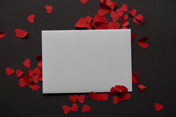 Top view of white empty greeting card and red paper cut hearts on black background — Stock Photo