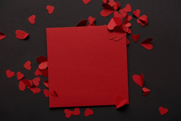 Top view of red blank greeting card and paper cut hearts on black background — Stock Photo