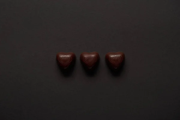Vista superior de corazones de chocolate dulce sobre fondo negro con espacio de copia - foto de stock