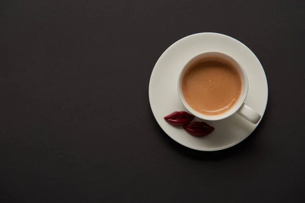 Draufsicht auf Tasse mit Kaffee und Schokolippen auf Untertasse auf schwarzem Hintergrund — Stockfoto