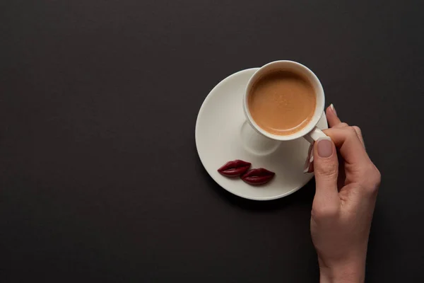 Vista superior de la mujer sosteniendo la taza de café cerca de los labios de chocolate en platillo - foto de stock