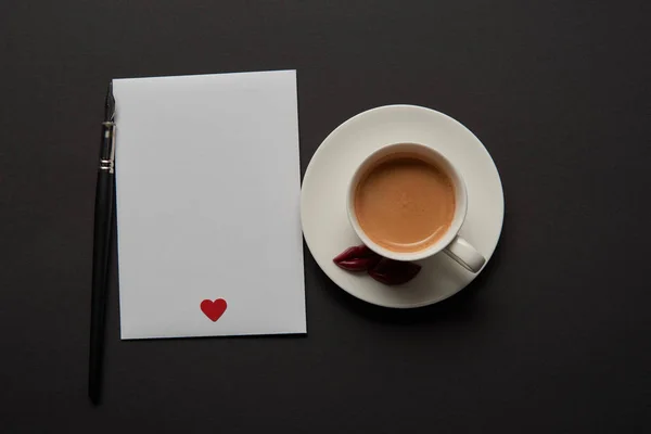 Vista superior de la tarjeta de felicitación vacía con el signo rojo del corazón cerca de la taza de café - foto de stock