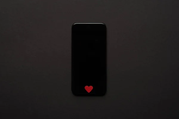 Vue du haut du smartphone avec écran vierge et petit signe de coeur rouge sur fond sombre — Photo de stock