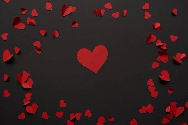 Vue de dessus des grands et petits coeurs rouges coupés en papier sur fond noir — Photo de stock
