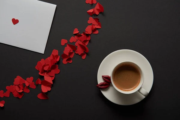 Vista superior de la tarjeta de felicitación blanca con corazones cortados de papel rojo y taza de café - foto de stock