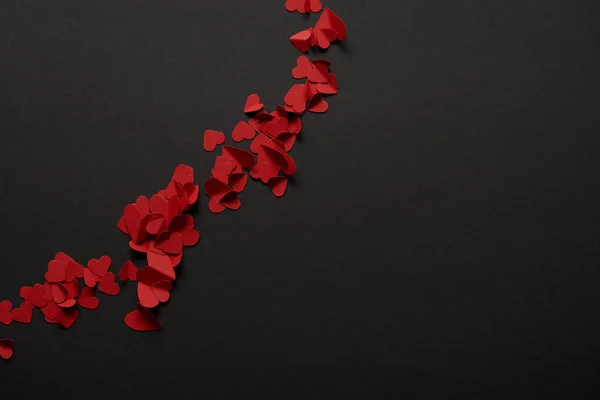 Vista dall'alto di rosso piccoli cuori tagliati carta su sfondo nero — Foto stock