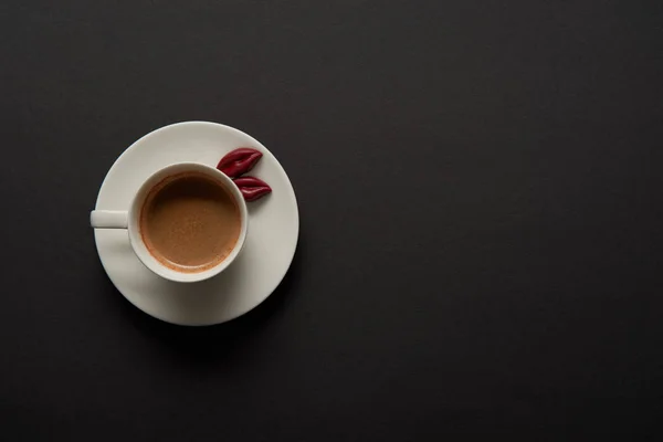 Vista superior da xícara de café com lábios de chocolate no pires no fundo preto — Fotografia de Stock