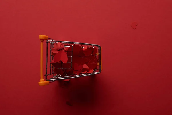 Top view of shopping cart with decorative paper cut hearts on red background — Stock Photo