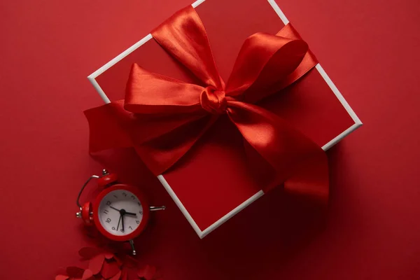 Top view of red present with silk ribbon, clock and paper cut hearts on red background — Stock Photo