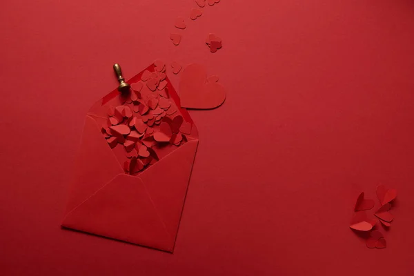 Vue du haut des coeurs coupés en papier et enveloppe ouverte sur fond rouge — Photo de stock