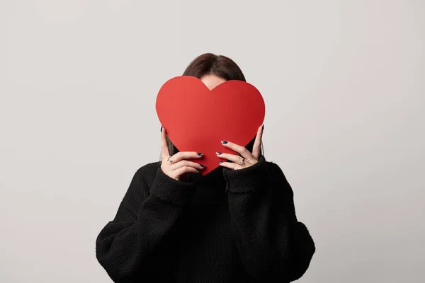 Girl in black with obscure face and empty paper cut heart card isolated on grey — Stock Photo