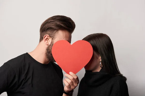 Joven pareja en negro con papel vacío corte tarjeta de corazón - foto de stock