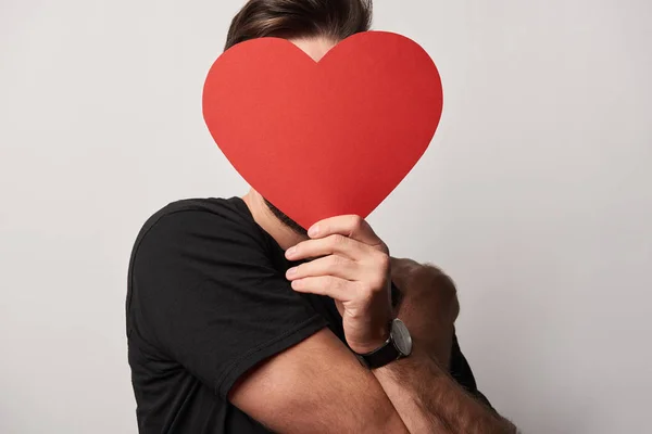 Hombre de negro con cara oscura y papel vacío tarjeta de corazón cortado - foto de stock