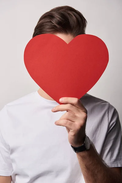 Hombre con cara oscura sosteniendo papel vacío tarjeta de corazón cortado aislado en gris - foto de stock
