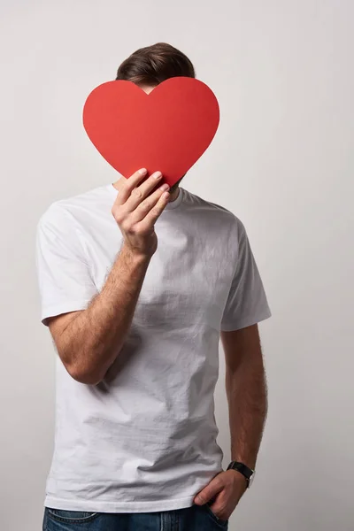 Mann mit undurchsichtigem Gesicht und einer Hand in der Tasche, die eine leere, papiergeschnittene Herzkarte hält — Stockfoto